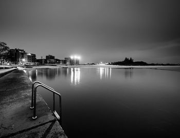 Illuminated buildings by river against sky at night