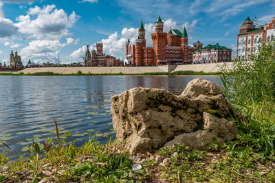 View of buildings by river against cloudy sky