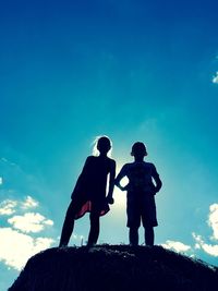 Silhouette friends standing on rock against sky