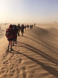 Rear view of people walking at desert against sky