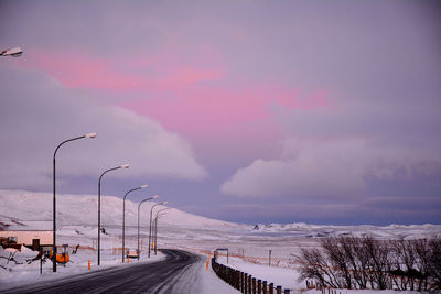 Road by snow covered street against sky during sunset