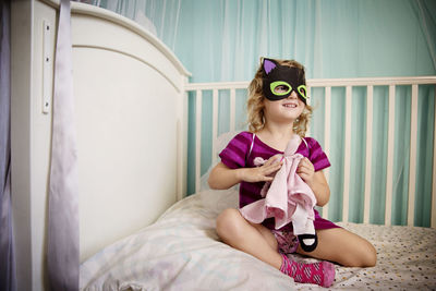 Cute girl wearing mask playing with doll while sitting in crib