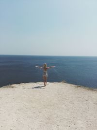 Rear view of woman with arms outstretched standing at beach against clear sky