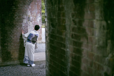 Rear view of woman in kimono against brick wall