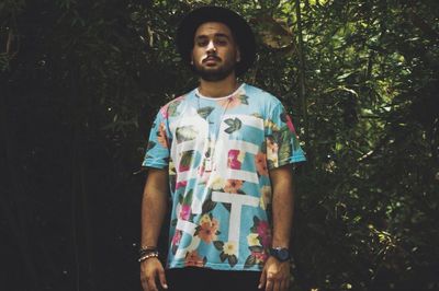 Portrait of young man wearing hat standing against plants in forest