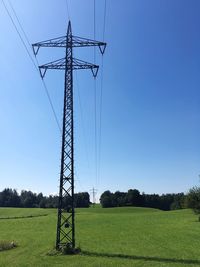 Electricity pylons on landscape against clear blue sky