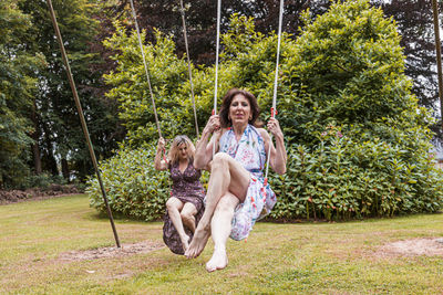 Beautiful middle aged couple of female friends swinging on children's swings in a french park