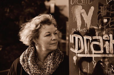 Close-up of thoughtful woman standing by graffiti wall