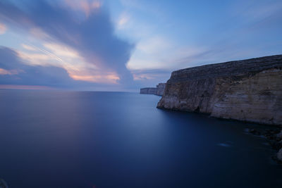 Scenic view of cliff at sea shore against sky during sunset