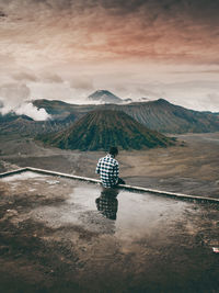 Man sitting at observation point against sky during sunset