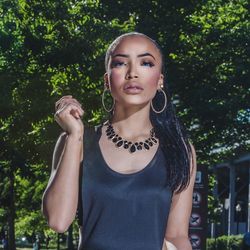 Portrait of beautiful young woman standing against trees