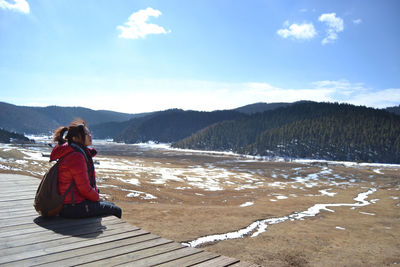 Woman sitting on snow covered mountain against sky