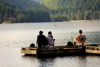 Rear view of people sitting on lake against trees