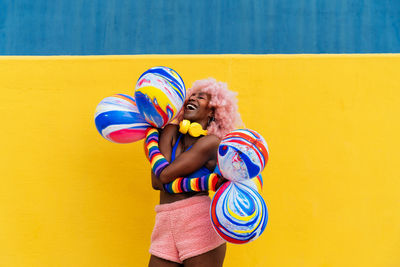 Rear view of woman with arms raised standing against yellow wall