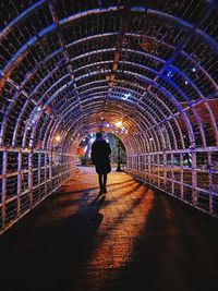 Rear view of man walking in illuminated tunnel