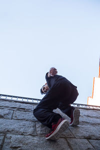 Full length portrait of man climbing on wall against clear sky