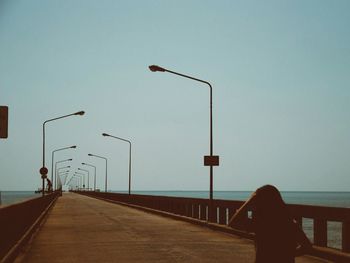 Rear view of people on railing by sea against clear sky