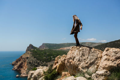 Man standing on rock by sea against clear sky