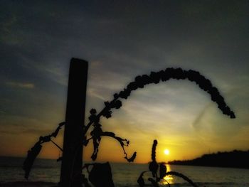 Silhouette wooden posts on beach against sky at sunset