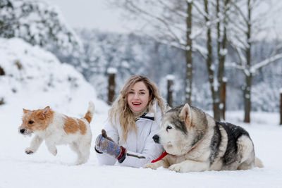 Portrait of woman with dogs sitting on snow covered land during winter