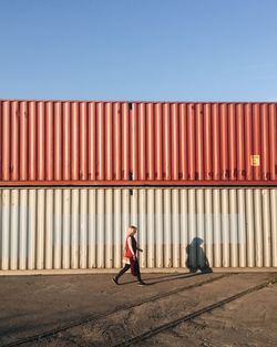 Full length of woman walking against cargo container during sunny day