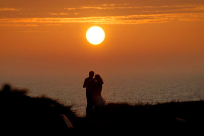 Silhouette people standing by sea against sky during sunset