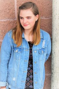 Teenage girl looking away while standing against wall