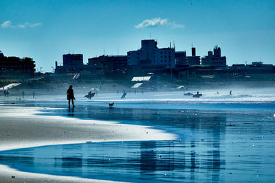 People on sea by buildings against sky in city