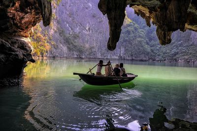 People traveling in boat on lake seen from cave