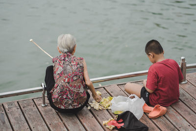 Rear view of senior woman by boy sitting on pier over lake
