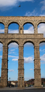 Bird flying with wings open above segovia viaduct with religious symbol, spain