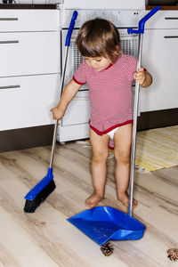 Full length of baby girl cleaning floor with broom at domestic kitchen