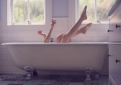 Low section of young woman in bathtub at home