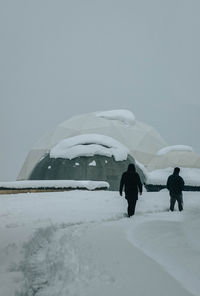 Rear view of man walking on snow covered landscape against clear sky