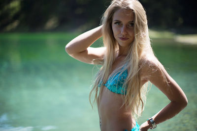 Portrait of young woman in bikini standing against lake