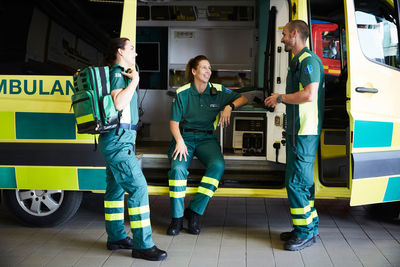 Female paramedic sitting in ambulance while talking with coworkers in parking lot