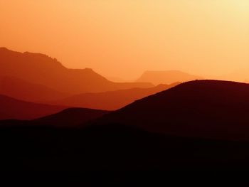 Scenic view of silhouette mountains against orange sky