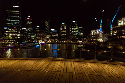 Illuminated buildings by river against sky at night