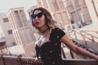 Portrait of young woman wearing sunglasses standing by railing in city