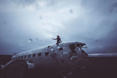 Woman sitting on abandoned airplane against sky