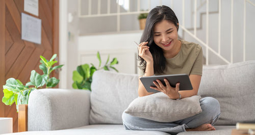 Young woman using phone while sitting on sofa at home