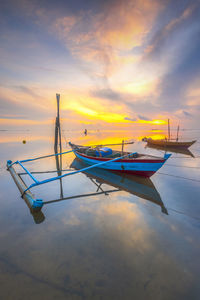 Boat moored on beach against sky during sunset