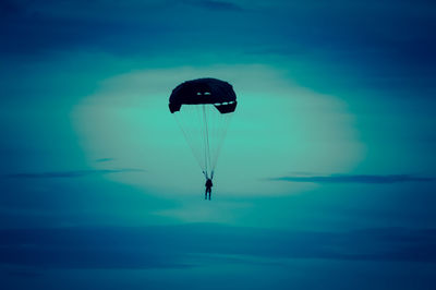 Silhouette person paragliding against blue sky
