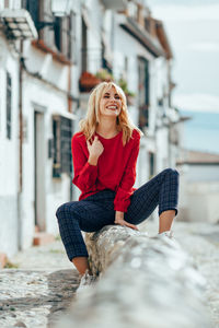 Smiling young woman sitting on footpath in city