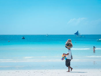 Man selling hats while walking on sand against sea at beach