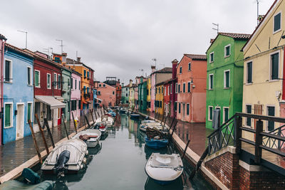 Boats moored in canal amidst buildings against sky