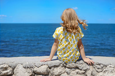 Rear view of woman on rock by sea against sky
