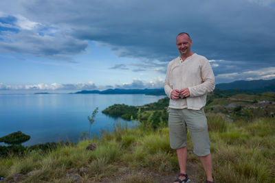 Portrait of smiling man standing on shore against cloudy sky