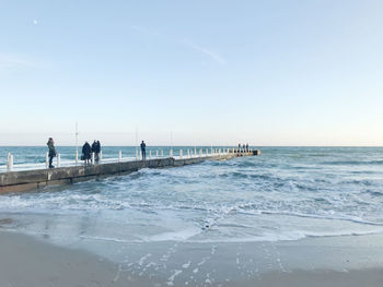 People on pier in sea against blue sky