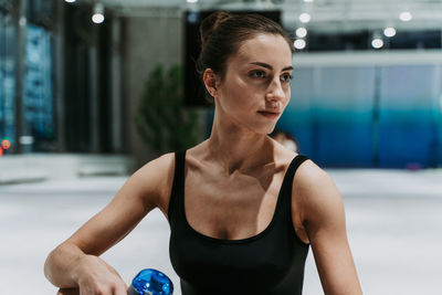 Smiling woman holding water bottle sitting at gym